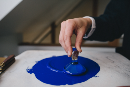 A person's hand using a paintbrush to mix blue watercolor paint on a palette.