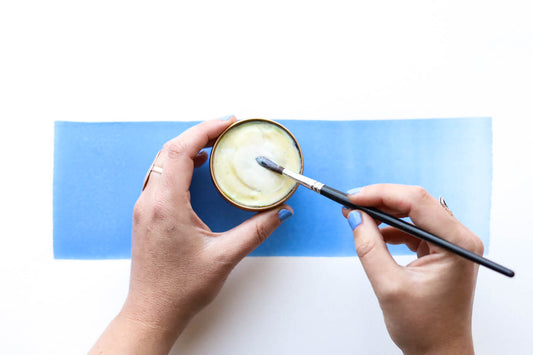An open Case for Making Brush Buddy in the process of being used.  Two hands shown, one holding the circular brush buddy and the other holding the brush being cleaned.